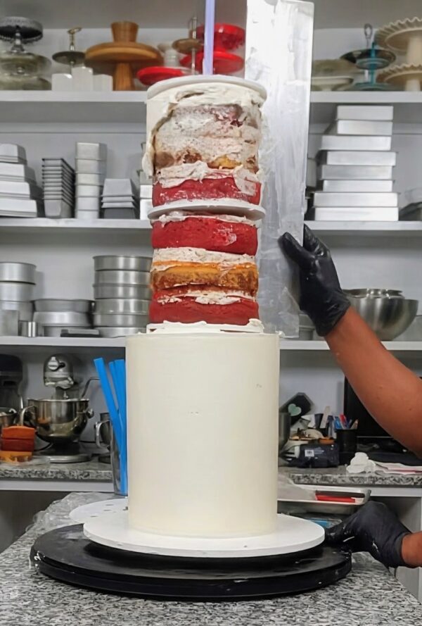 Decorator stacking a second cake tier while the acrylic cake frosting ring stays in place to prevent smudging.